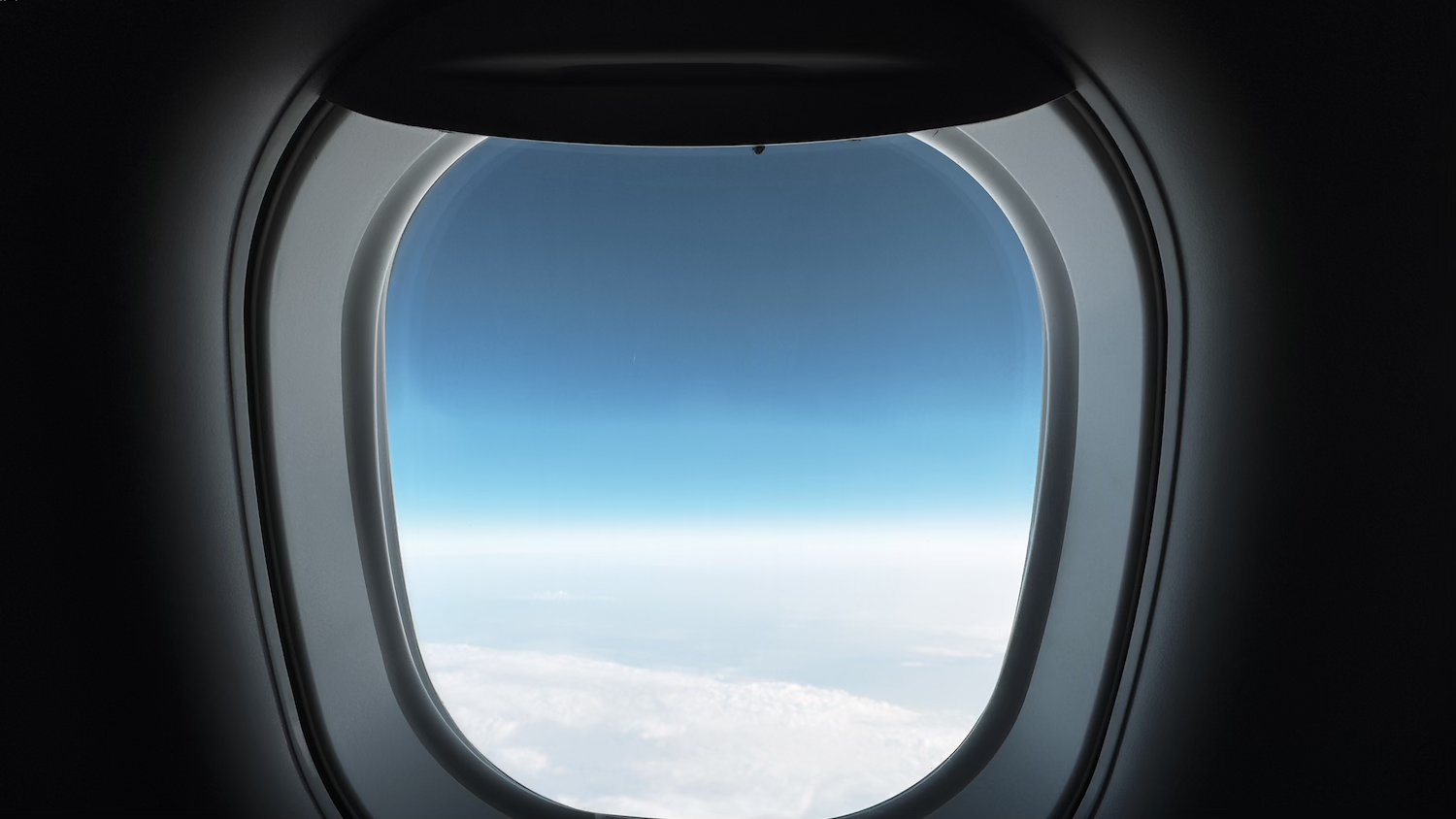 An image of An airplane window looking out to cloudy skies.