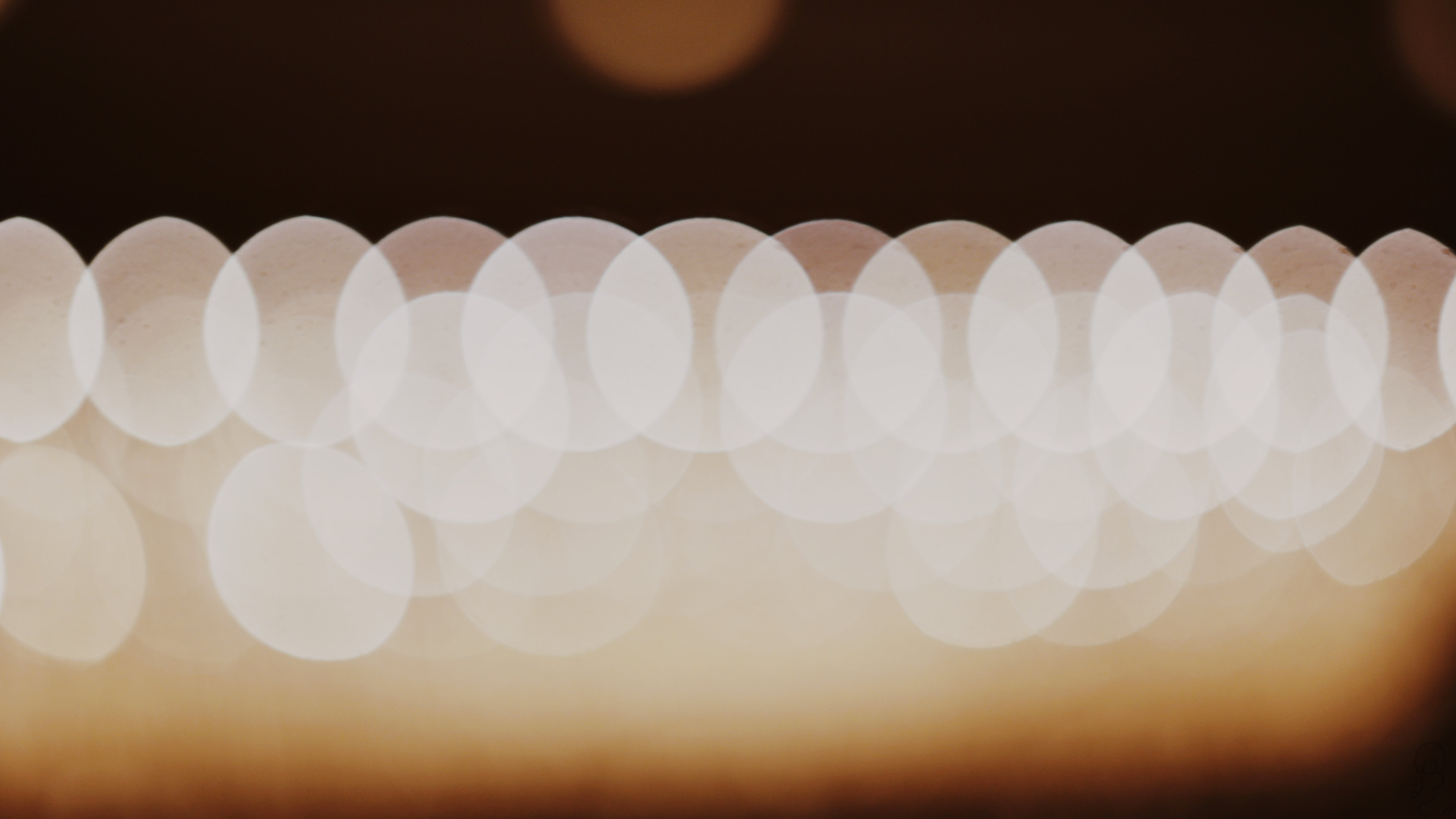 An image of A series of brown and white balls of light on a black background, the result of intentionally defocusing the lens against a chandelier