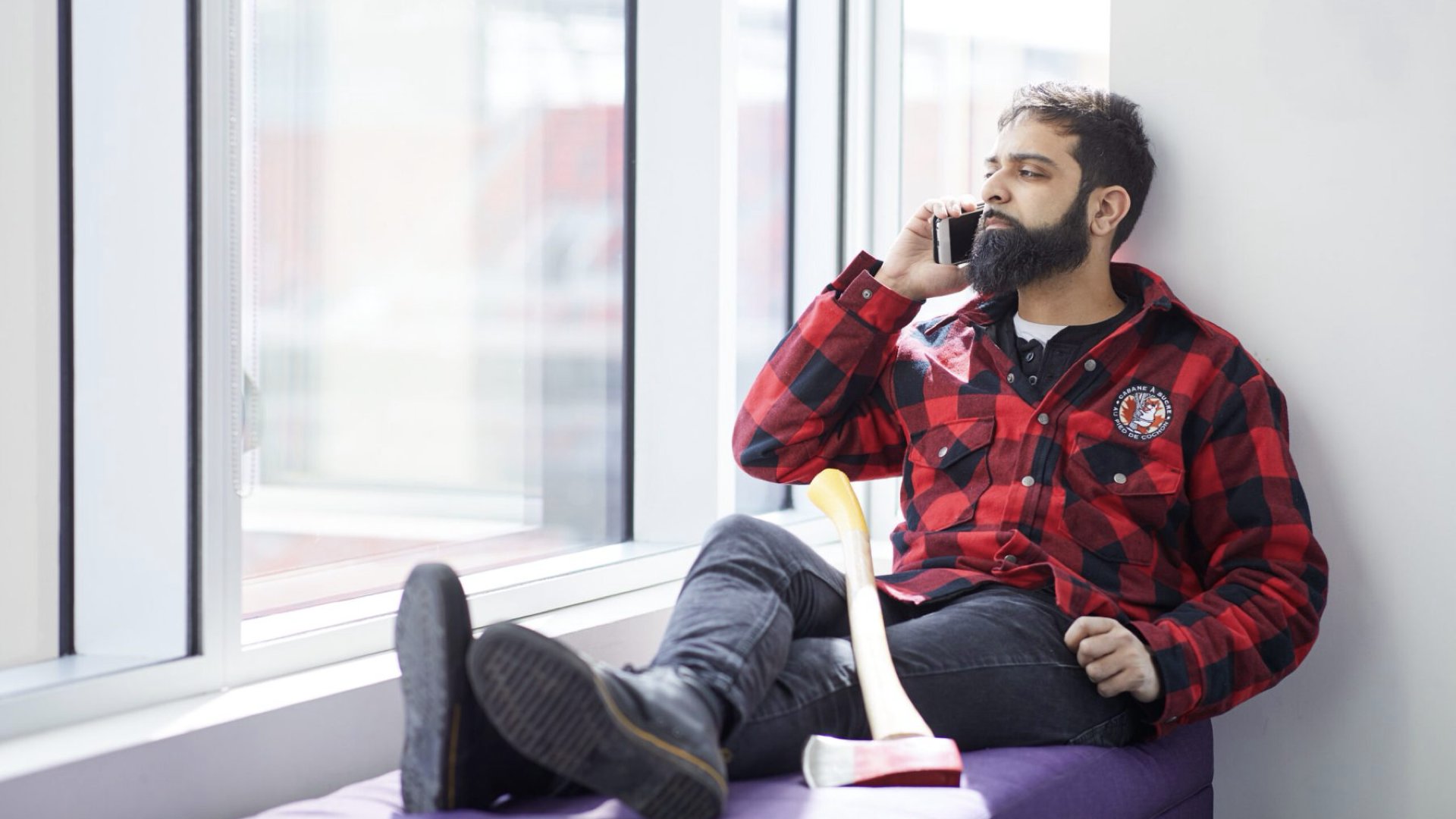 A very Canadian person lazing back on a chair talking on a cell phone with an axe to his side. Photo credit: CIRA stock photos.